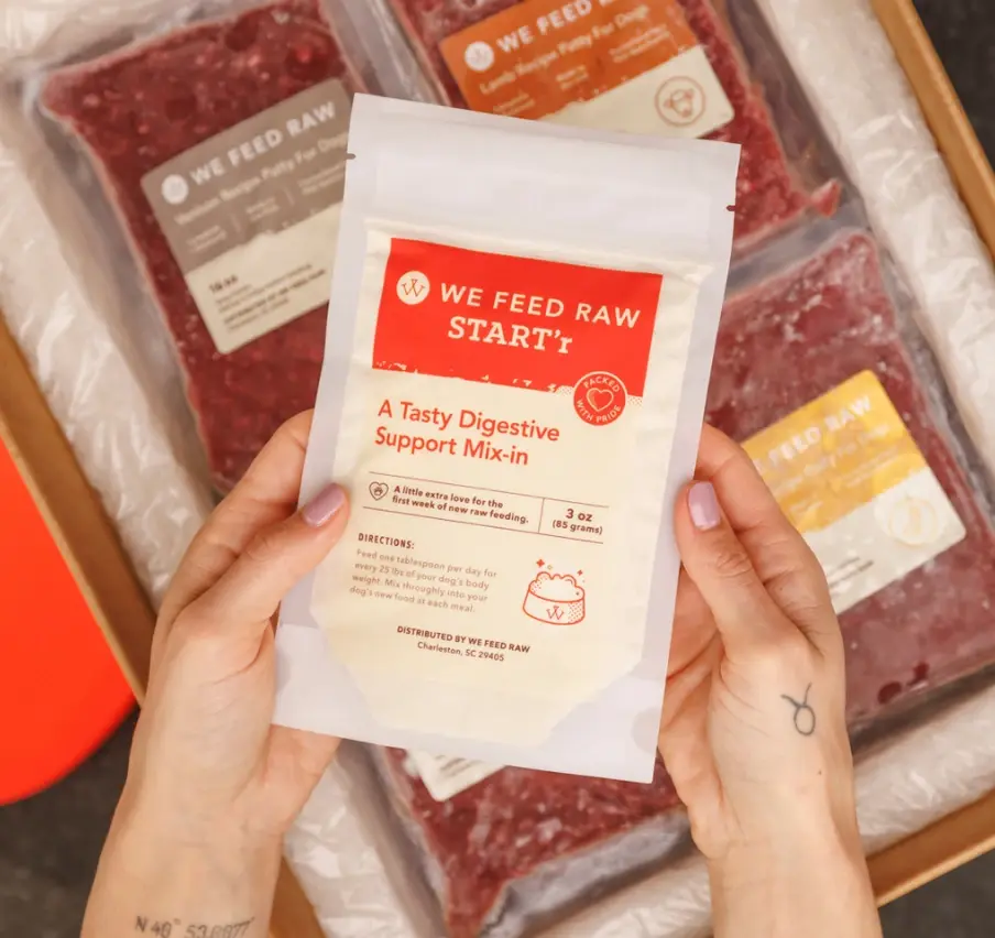 A package of We Feed Raw START'r, labeled as 'A Tasty Digestive Support Mix-in'. The package indicates it's 3 oz (85 grams) and provides 'A little extra love for the first week of new raw feeding.' Directions state: 'Feed one tablespoon per day for every 25 lbs of your dog's body weight. Mix thoroughly into your dog's new food at each meal.' The product is distributed by We Feed Raw in Charleston, SC 29405.